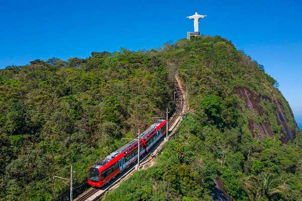 Trem do Corcovado sobe a encosta com o Cristo Redentor ao fundo
